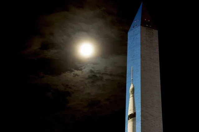 The moon is visible through clouds, left, as an image of a 363-foot Saturn V rocket is projected on the east face of the Washington Monument in Washington, Wednesday, July 17, 2019, in celebration of the 50th anniversary of the Apollo 11 moon landing. (Photo by Andrew Harnik/AP Photo)