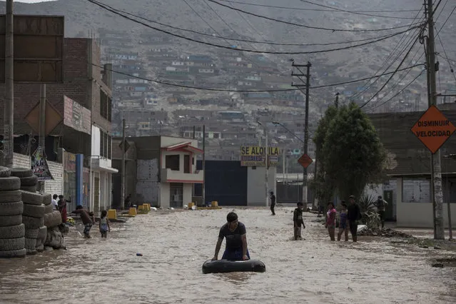 A man plays in a flooded street using an inner tube in Lima, Peru, Thursday, March 16, 2017. Muddy water spilled onto streets and into homes on Thursday in a new round of unusually heavy rains that has killed at least a dozen people in Peru and now threatens flooding in the capital. The intense rains and mudslides over the past three days have wrought havoc around the Andean nation and caught residents in Lima, a desert city of 10 million where it almost never rains, by surprise. In one of the more dramatic incidents, stunned residents watched and took out cellphone cameras as a woman escaped after being swept into an avalanche of mud, wood debris and farm animals about 53 kilometers (32 miles) south of downtown Lima. Authorities said Thursday they expect the rains caused by El Nino, which generates a warming of surface waters in the eastern Pacific Ocean, to continue for another two weeks. Thus far, officials say a total of 62 people have died and 12,000 homes have been destroyed in storms this year. President Pedro Pablo Kuczynski said late Wednesday that authorities are prepared to provide shelter and relief to those left homeless. (Photo by Rodrigo Abd/AP Photo)