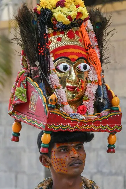 A devotee worshipping Hindu Goddess Marammadevi, an incarnation of Shakthi, carries the mask of the Goddess on his head as he seeks alms in Bangalore on January 29, 2022. (Photo by Manjunath Kiran/AFP Photo)