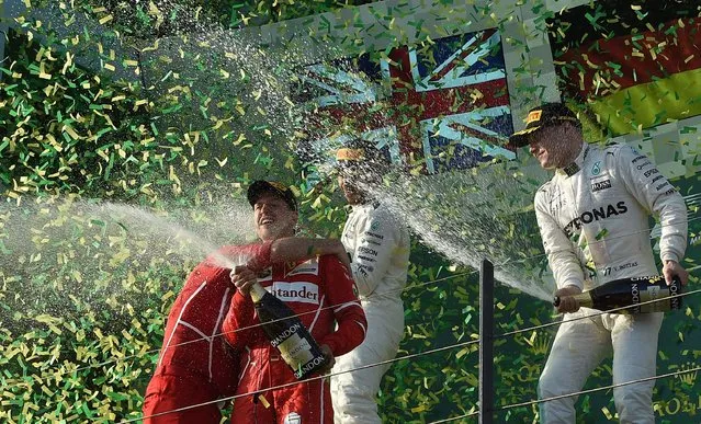 Ferrari's German driver Sebastian Vettel (2nd L) is soaked with champagne by third-placed Mercedes' Finnish driver Valtteri Bottas (R) and runner-up Mercedes's British driver Lewis Hamilton (2nd R) as Ferrari's trackside engineering team member Luigi Fraboni (L) embraces him, after his victory in the Formula One Australian Grand Prix in Melbourne on March 26, 2017. (Photo by Paul Crock/AFP Photo)
