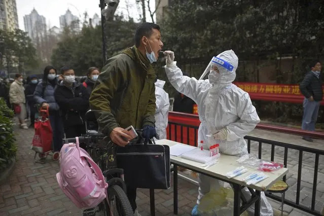 A man holding his bicycle with a school bag on it gets a throat swab during a mass COVID-19 test at a residential compound in Wuhan in central China's Hubei province, Tuesday, February 22, 2022. Wuhan, the first major outbreak of the coronavirus pandemic has reported more than dozen new coronavirus cases this week, prompting the authority to step up precautious measures. (Photo by Chinatopix via AP Photo)