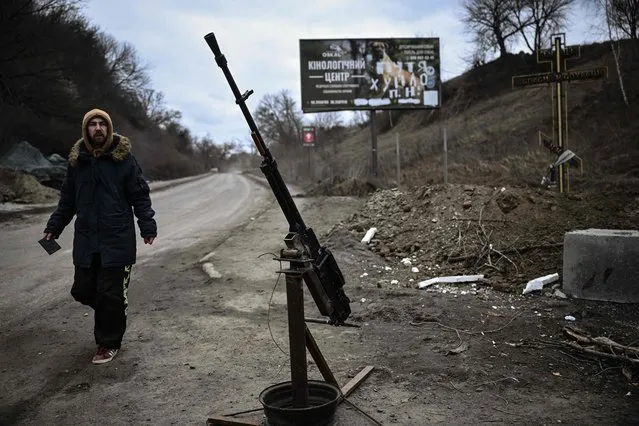 A man walks past a machine gun at a checkpoint next to the last bridge on the road that connects Stoyanka with Kyiv, on March 6, 2022. (Photo by Aris Messinis/AFP Photo)