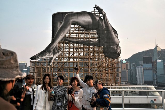 People take pictures with public art instalation titled “GIANTS: Rising Up” by the French artist JR, at Harbour City, Hong Kong, China on March 16, 2023. (Photo by Lam Yik/Reuters)