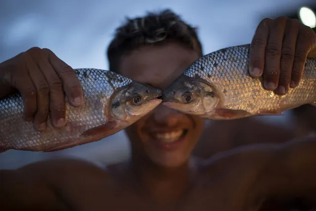 A young vendor holds a pair of fish to his face as he jokingly poses for a photo at the Panair fish market in Manaus, Brazil, on May 24, 2014. (AP Photo/Felipe Dana)