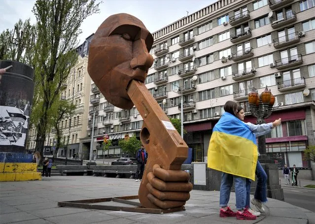 Women wrapped in the Ukrainian national flag take selfies near an installation depicting Russian President Vladimir Putin with a gun in his mouth and writing “Shoot yourself” in central Kyiv, Ukraine, Saturday, May 7, 2022. (Photo by Efrem Lukatsky/AP Photo)