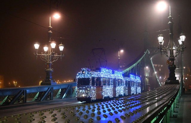 A picture taken on December 19, 2023 shows a Ganz UV type tram of the Budapest Transport Privately Held Corporation decorated with Christmas lights, as it drives through the Freedom Bridge in Budapest, Hungary. The decorated tram operates through Christmas until the New Year season. (Photo by Attila Kisbenedek/AFP Photo)