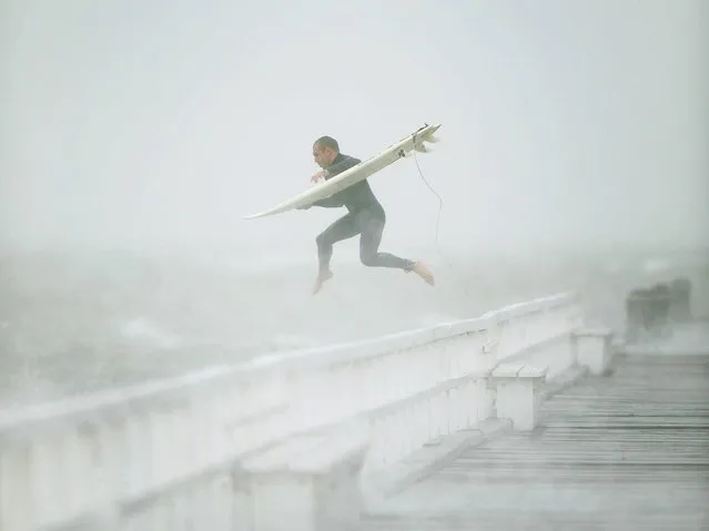 A surfer jumps off the pier into Port Phillip Bay to take advantage of the waves as a storm lashes the Melbourne area on June 24, 2014. (Photo by Mal Fairclough/AFP Photo)