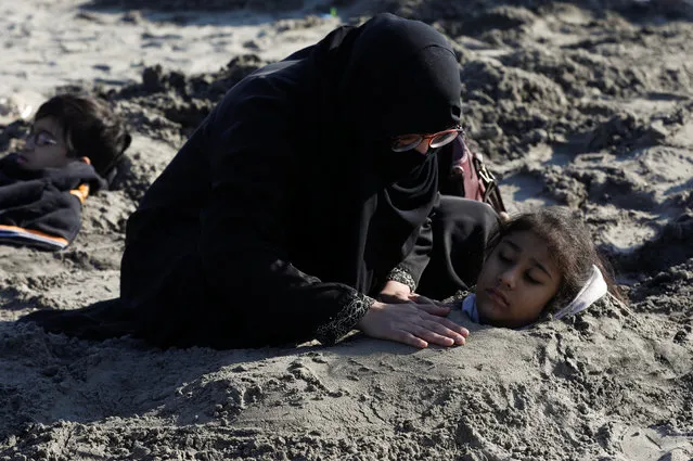 A woman comforts her daughter, buried up to her neck in sand during a solar eclipse, along Clifton beach in Karachi, Pakistan on December 26, 2019. Many Pakistanis believe that burying people with disabilities in sand during solar eclipse would bring healing to their bodies. (Photo by Akhtar Soomro/Reuters)