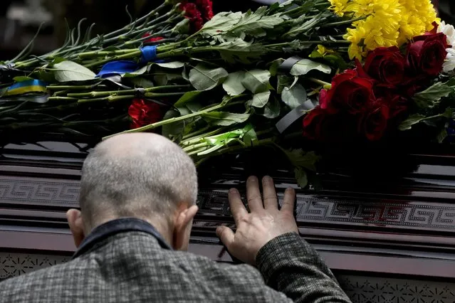A man touches the coffin with the remains of activist and soldier Roman Ratushnyi during his funeral in Kyiv, Ukraine, Saturday, June 18, 2022. (Photo by Natacha Pisarenko/AP Photo)