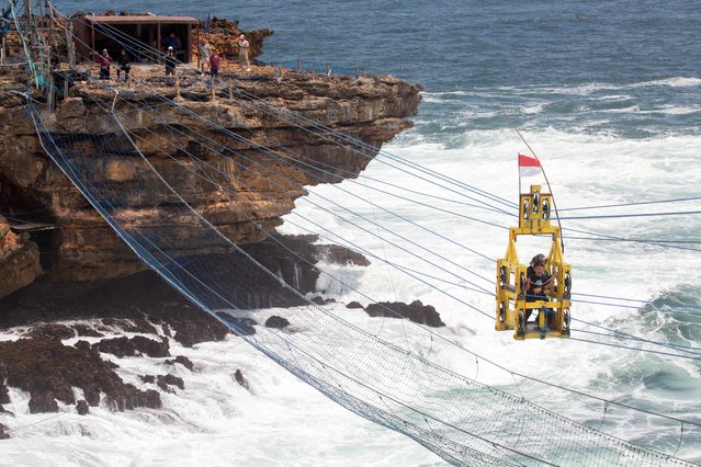 Tourists ride in a human-powered gondola lift to cross the 120-metre-long distance to Karang Watu Panjang Island, a popular tourist attraction, at Timang Beach, Gunung Kidul, Yogyakarta, October 5, 2024. (Photo by Devi Rahman/AFP Photo)