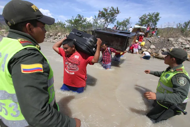 Colombian police watch people carry their household belongings across the Tachira River from Venezuela, top, to Colombia, on the border that separates San Antonio del Tachira, Venezuela from Villa del Rosario, Colombia, Tuesday, August 25, 2015, during a mass exodus of Colombians. (Photo by Eliecer Mantilla/AP Photo)