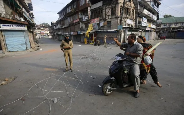 A Police officer stops a Kashmiri motorist  near barbed wire barrier in Srinagar, the summer capital of Indian Kashmir, 11 July 2016. A curfew remained in place in most parts of Indian Kashmir for the third consecutive day as authorities struggled to contain protests following the killing of top militant commander Burhan Muzaffar Wani. According to local news the death toll reached 23 including 22 civilians and one policeman while three policemen are missing and over 200 persons were injured during clashes. (Photo Farooq Khan/EPA)