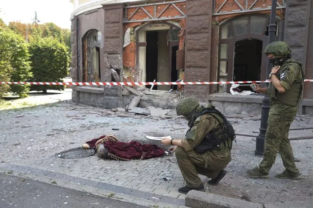 Investigative committee officers inspect an area of shelling as a lifeless body lies covered on the ground, in Donetsk, which is under control of the Government of the Donetsk People's Republic, eastern Ukraine, Thursday, August 4, 2022. (Photo by AP Photo)