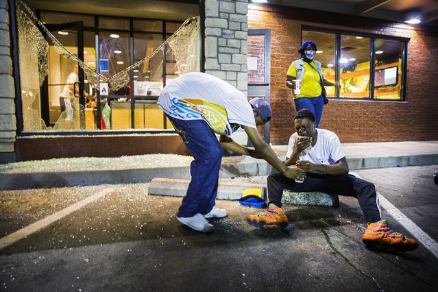 Protesters react to the effects of tear gas which was fired at demonstrators reacting to the shooting of Michael Brown in Ferguson, Missouri August 17, 2014. Shots were fired and police shouted through bullhorns for protesters to disperse, witnesses said, as chaos erupted Sunday night in Ferguson, Missouri, which has been racked by protests since the unarmed black teenager was shot by police last week. (Photo by Lucas Jackson/Reuters)