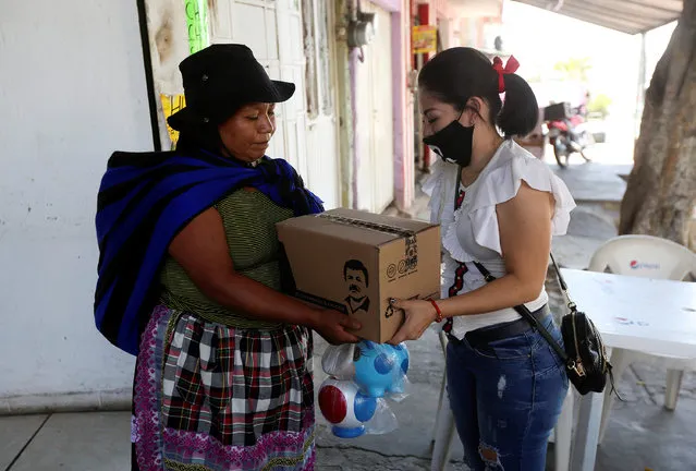An employee of the clothing brand “El Chapo 701”, owned by Alejandrina Gisselle Guzman, daughter of the convicted drug kingpin Joaquin “El Chapo” Guzman, hands out a box with food, face masks and hand sanitizer to an elderly woman as part of a campaign to help cash-strapped elderly people during the coronavirus disease (COVID-19) outbreak, in Guadalajara, Mexico April 16, 2020. The number 701 refers to the 2009 World's Billionaires ranking given by Forbes magazine to Mexican drug lord Joaquin “El Chapo” Guzman. (Photo by Fernando Carranza/Reuters)