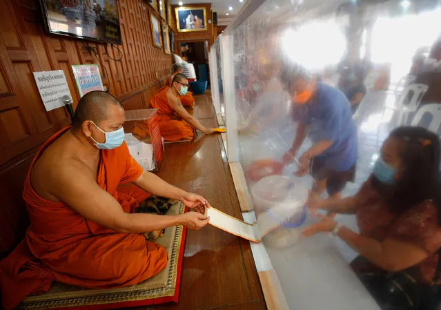 Thai Buddhist monks wear protective masks while receiving devotees offerings, behind plastic sheets set up to reduce the risk of coronavirus and COVID-19 infections, during the Songkran celebrations at Wat Samian Nari in Bangkok, Thailand, 14 April 2020. The Songkran Festival was canceled nationwide for prevent the spread of the COVID-19 disease, caused by the SARS CoV-2 coronavirus. Usually the Songkran Festival is held for three days to mark the Thai traditional New Year, falling annually on 13 April. (Photo by Narong Sangnak/EPA/EFE/Rex Features/Shutterstock)