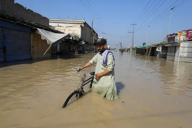 A man walks with a bicycle in flood water following rains and floods during the monsoon season in Nowshera, Pakistan on August 29, 2022. (Photo by Fayaz Aziz/Reuters)