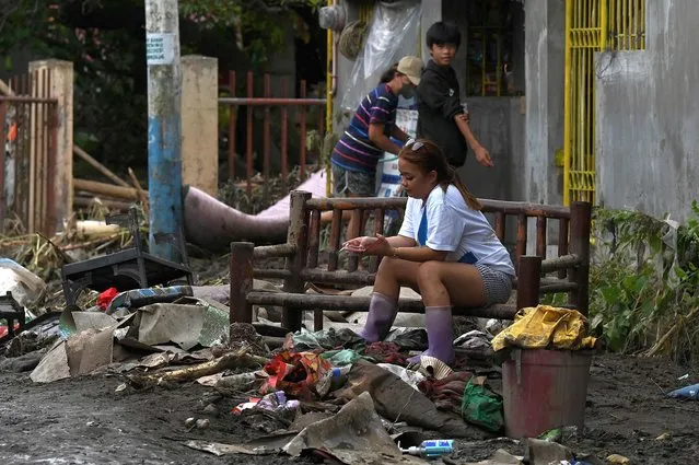 A woman sits on a bench along a mud-covered street in Noveleta, Cavite on October 30, 2022, a day after Tropical Storm Nalgae hit. Emergency workers scrambled to rescue residents trapped by floods in and around the Philippine capital on October 30 as Tropical Storm Nalgae swept out of the country after killing at least 48 people. (Photo by Jam Sta Rosa/AFP Photo)