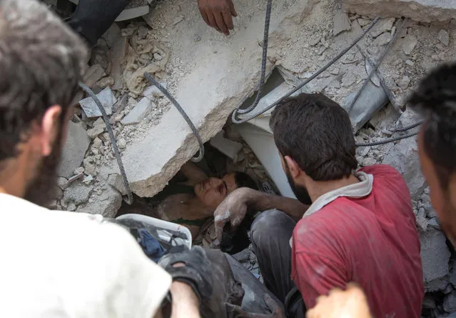 Syrian civil defence volunteers, known as the White Helmets, dig out a young boy trapped under the rubble of destroyed buildings following reported air strikes on the rebel-held neighbourhood of Al-Mashhad in the northern city of Aleppo, on July 25, 2016. Air strikes and barrel bomb attacks killed 16 civilians in rebel-held parts of Aleppo province, with rebel rocket fire onto government areas killing three more, the Britain-based Syrian Observatory for Human Rights said. (Photo by Karam Al-Masri/AFP Photo)