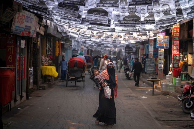 A woman walks with a child in her arms along a street with election campaign posters hanging in Dhaka, Bangladesh, Friday, January 5, 2024. (Photo by Altaf Qadri/AP Photo)
