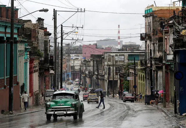 People walk as cars are driven on a street during rain in Havana, Cuba, August 30, 2016. (Photo by Enrique de la Osa/Reuters)