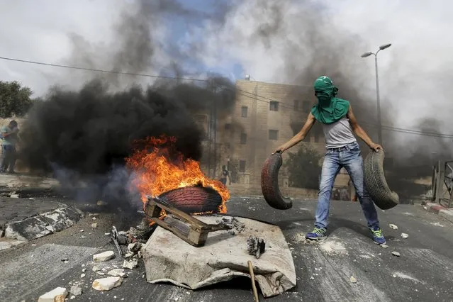 A masked Palestinian youth adds tyres to a fire during clashes with Israeli police in Sur Baher, a village in the suburbs of Arab east Jerusalem, October 7, 2015. A suspected Palestinian militant stabbed and wounded an Israeli soldier, snatched his gun and was then shot dead by special forces on Wednesday, police said, as a surge of violence prompted Israel's prime minister to cancel a visit to Germany. (Photo by Ammar Awad/Reuters)