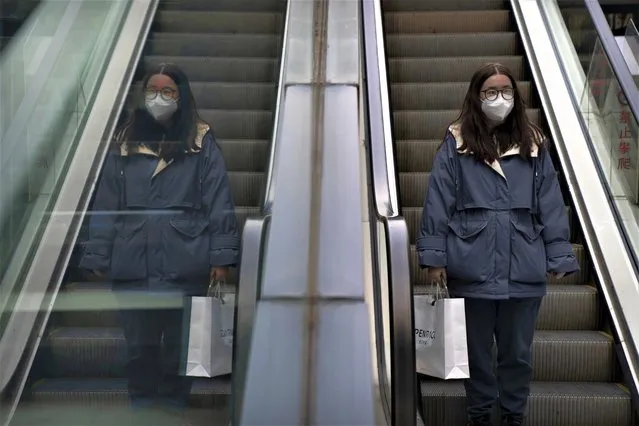 A woman wearing a face mask rides an escalator at a shopping and office complex in Beijing, Wednesday, January 11, 2023. Japan and South Korea on Wednesday defended their border restrictions on travelers from China, with Tokyo criticizing China's move to suspend issuing new visas in both countries as a step unrelated to virus measures. (Photo by Mark Schiefelbein/AP Photo)