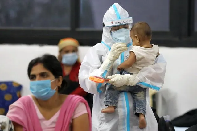 A medical worker in personal protective equipment (PPE) plays with a child of woman recovering inside a quarantine centre for the coronavirus disease (COVID-19) patients amidst the spread of the disease at an indoor sports complex in New Delhi, India, September 22, 2020. (Photo by Anushree Fadnavis/Reuters)