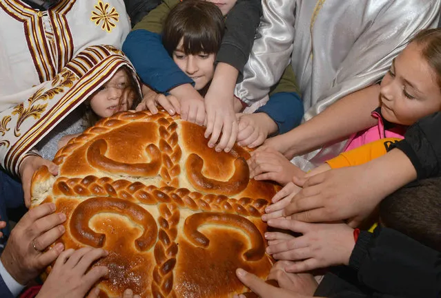 Children and priest break traditional Christmas bread to mark the Orthodox Christmas Day festivities in the Bosnian town of Banja Luka, 240 kms northwest of Sarajevo, Saturday, January 7, 2023. Children traditionally scramble for a piece of the bread, searching for a gold coin, hidden inside. (Photo by Radivoje Pavicic/AP Photo)