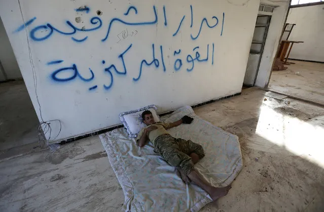 A rebel fighter of the 'Sham Legion' rests inside the institution of religious law building that was used by Islamic State militants in the northern Syrian rebel-controlled town of al-Rai, in Aleppo Governorate, Syria, September 27, 2016. The arabic reads: “Ahrar al-Shariqya (a rebel group), the central force”. (Photo by Khalil Ashawi/Reuters)