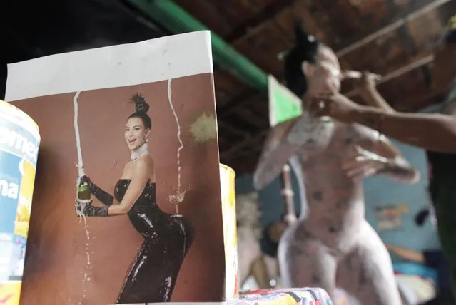 A photograph of TV celebrity Kim Kardashian stands in between two pots of paint, as Adriana Ramirez (partially obscured) paints a pinata depicting Kardashian at her brother's workshop in Reynosa December 6, 2014. (Photo by Daniel Becerril/Reuters)