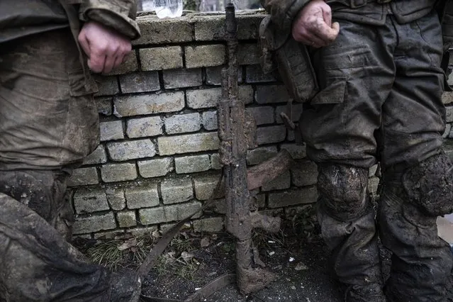 A mud-stained gun is seen in front of Ukrainian servicemen which just come back from tranches of Bakhmut in Chasiv Yar, Ukraine, Wednesday, March 8, 2023. (Photo by Evgeniy Maloletka/AP Photo)