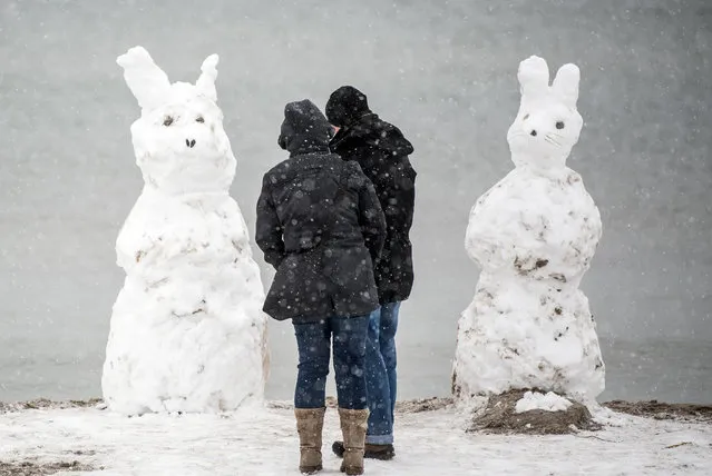 A man and a woman stand in front of two “snow hares” on the island Fehmarn, northern Germany, on April 1, 2018. (Photo by Federico Gambarini/AFP Photo/DPA)