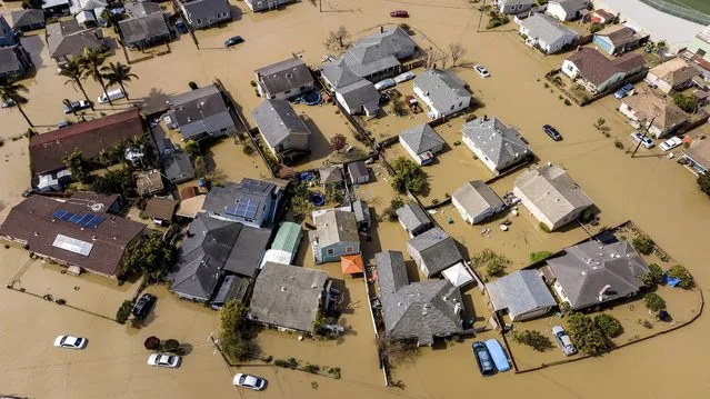 Floodwaters surround homes and vehicles in the community of Pajaro in Monterey County, Calif., on Monday, March 13, 2023. Built in the late 1940s to provide flood protection, the Pajaro River's levee has been a known risk for decades with several breaches in the 1990s. Emergency repairs to a section of the berm were undertaken in January. (Photo by Noah Berger/AP Photo)