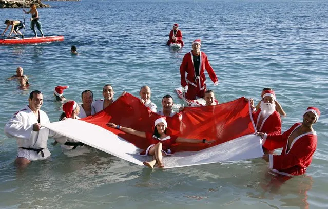 Swimmers dressed as Santa Claus pose for photographers with a Monaco flag during the traditional Christmas season swim in Monaco December 21, 2014. A hundred swimmers took part in the yearly event in the Mediterranean Sea waters which measured 16 degrees Celsius (60 degrees Fahrenheit). (Photo by Eric Gaillard/Reuters)