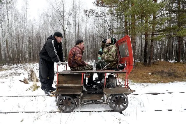 (L-R) A man nicknamed "Barcelona", Alexey Bolotov and Alexey Jakushin drink vodka as they travel by a pioneer motorised railcar on their way to Kalach, Sverdlovsk region, Russia October 18, 2015. The "pioneer," a light auxiliary rail vehicle, is a popular form of transport among people who live along the Alapayevsk railway. (Photo by Maxim Zmeyev/Reuters)