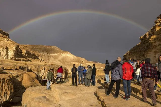 A rainbow forms as Israelis wait for a flash-flood to take place in the Negev desert East of the Israeli city of Dimona on December 26, 2022, following heavy rainfall over the region. (Photo by Menahem Kahana/AFP Photo)