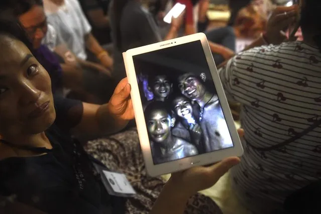 A family member shows a picture of four of the twelve missing boys near the Tham Luang cave at the Khun Nam Nang Non Forest Park in Mae Sai on July 2, 2018. Twelve boys and their football coach trapped in a flooded Thai cave for nine days were “found safe” on late July 2, in a miracle rescue after days of painstaking searching by divers. (Photo by Lillian Suwanrumpha/AFP Photo)