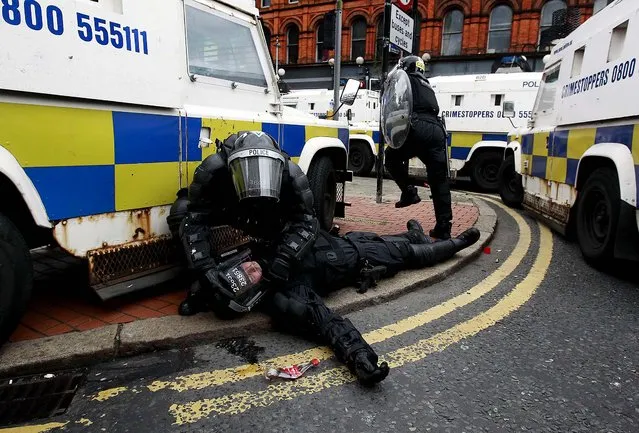 A police officer is tended to by a colleague after Loyalist protesters attacked the police with bricks and bottles as they waited for a republican parade to make its way through Belfast City Centre, on August 9, 2013. Police said two officers were injured. Eight were hurt the previous night when a crowd threw paint bombs, bottles and masonry at police. (Photo by Cathal McNaughton/Reuters)