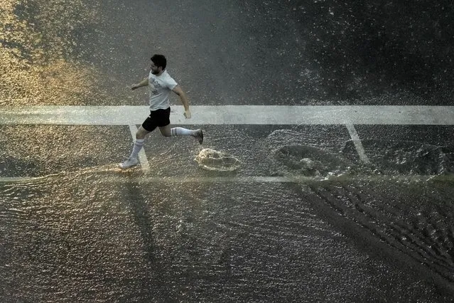 A pedestrian crosses a street in the rain as a severe thunderstorm passes through downtown Kansas City, Mo., Friday, July 14, 2023. (Photo by Charlie Riedel/AP Photo)