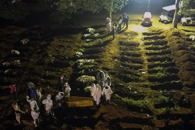 In this aerial view cemetery workers carry a coffin during the first burial at night amid the coronavirus (COVID-19) pandemic at the Vila Formosa cemetery in Sao Paulo, Brazil, on March 25, 2021. Brazil surpassed 100,000 new Covid-19 cases in one day on Thursday, adding another grim record in country where the pandemic has killed more than 300,000 people, the health ministry said. (Photo by Miguel Schincariol/AFP Photo)
