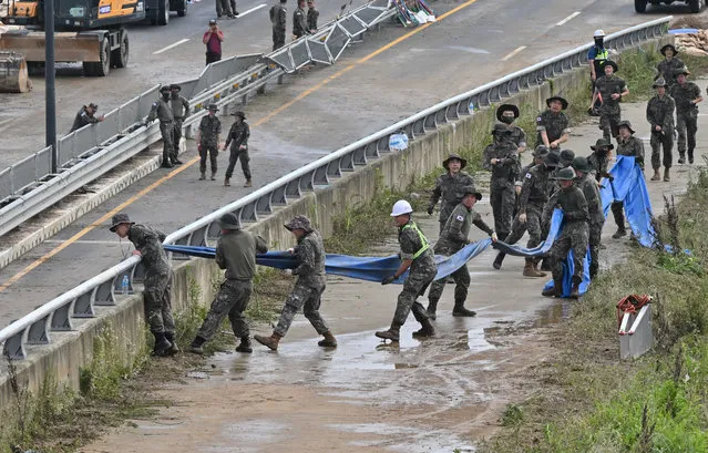 South Korean soldiers carry a tube to pump water out of a tunnel along a road leading to an underground tunnel where some 15 cars were trapped in flood waters after heavy rains in Cheongju on July 16, 2023. Rescuers battled to reach people trapped in a flooded tunnel on July 16, in South Korea, where at least 33 people have died and 10 are missing after heavy rains caused flooding and landslides. (Photo by Jung Yeon-Je/AFP Photo)