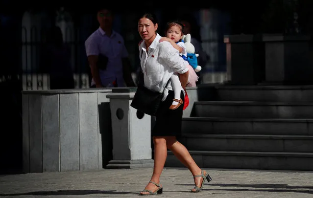 A woman carries her daughter as she waits to cross a street in Pyongyang, North Korea on September 8, 2018. (Photo by Danish Siddiqui/Reuters)