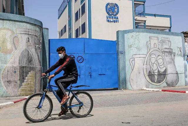 A Palestinian rides a bicycle past the closed gate of a school run by the United Nations Relief and Works Agency for Palestinian Refugees (UNRWA) in the city of Rafah in the southern Gaza Strip on April 6, 2021, amidst a lockdown due to the COVID-19 coronavirus pandemic. (Photo by Said Khatib/AFP Photo)