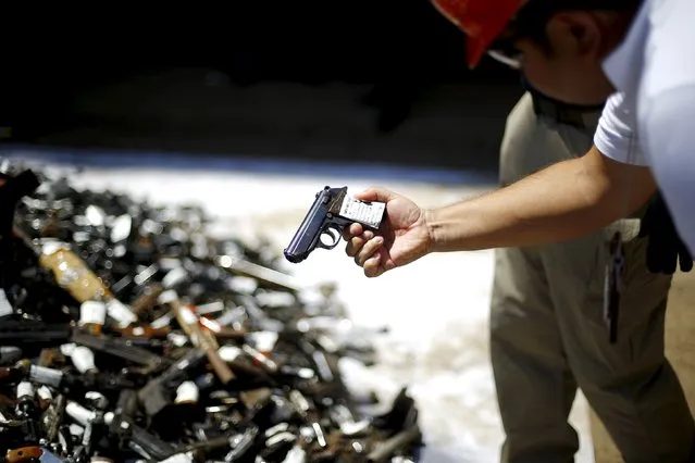 A policeman inspects a pile of confiscated weapons before they were destroyed at a foundry in Santiago, Chile, January 18, 2016. (Photo by Ivan Alvarado/Reuters)