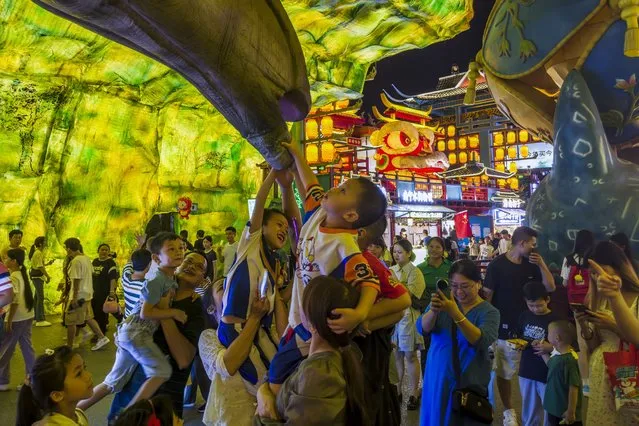 Visitors lift their children to torch a dinosaur figure on display in a new night market during a weeklong national holiday in Nanning in south China's Guangxi Zhuang Autonomous Region on September 30, 2023. (Photo by Chinatopix via AP Photo)