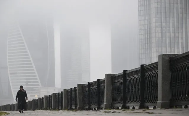 A woman walks along an embankment of the Moskva river in front of the buildings of Moscow's International Business Centre (Moskva City) on a foggy day in Moscow on October 23, 2023. (Photo by Alexander Nemenov/AFP Photo)
