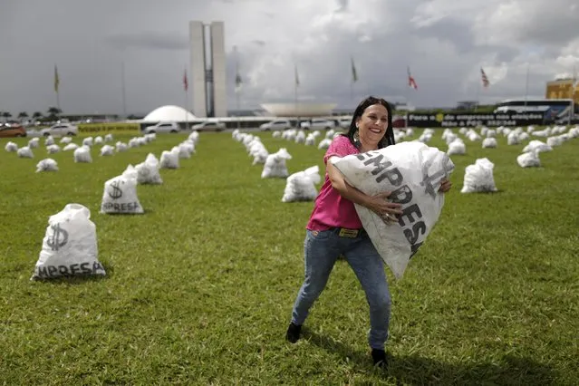 A woman carries a replica of a bag full of money in front of the National Congress during a protest symbolizing the donations of private companies for election campaigns, in Brasilia March 24, 2015. The protest was organized by the Coalition for Political Reform, a group formed by 101 Brazilian entities including the National Conference of Bishops of Brazil, Lawyers Association of Brazil and Landless Workers' Movement. (Photo by Ueslei Marcelino/Reuters)