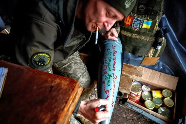 Oleksandr, 45, commander of an artillery unit, writes the name of a brother-in-arms killed in action on a howitzer shell at a position near a front line in the Donetsk region on November 4, 2023. (Photo by Alina Smutko/Reuters)