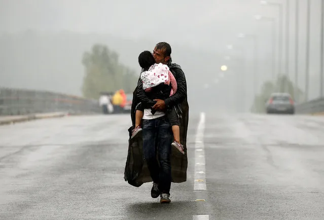 A Syrian refugee kisses his daughter as he walks through a rainstorm towards Greece's border with Macedonia, near the Greek village of Idomeni, September 10, 2015. (Photo by Yannis Behrakis/Reuters)